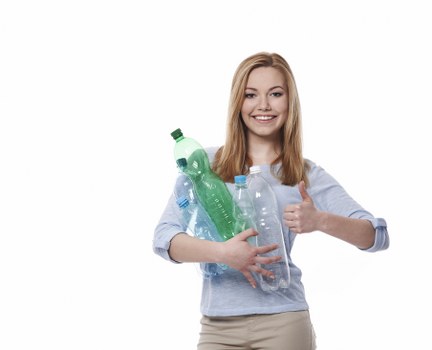 A young woman with long blonde hair and a friendly expression is standing against a plain white background. She is wearing a light blue, long-sleeved shirt with the sleeves rolled up and beige trousers. In her arms, she is holding several clear plastic bottles of varying sizes, some with green or blue caps, which appear to be empty or partially filled with liquids. She is giving a thumbs-up with her right hand, indicating approval or encouragement, and her overall posture and facial expression convey positivity. The bottles are positioned at chest level, with some slightly leaning to the side. The scene is well-lit, with even lighting that highlights the transparent and smooth textures of the plastic bottles and the soft fabric of her clothing. This image is suitable for illustrating topics related to recycling, waste awareness, or environmental responsibility, aligning with the waste management services provided by Commercial Waste Removal Covent Garden, in the context of promoting responsible rubbish disposal practices in the local area.